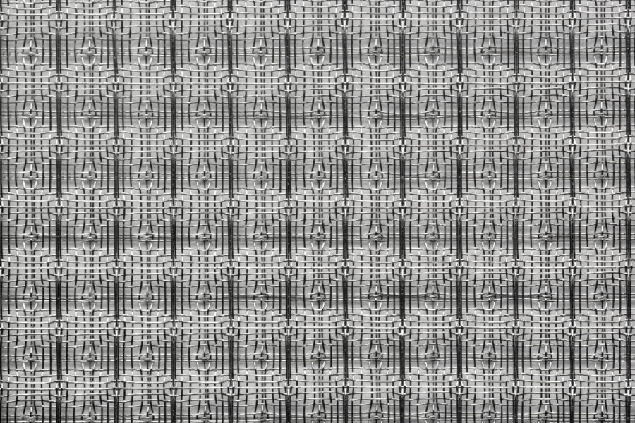 Pattern di tessuto in bianco e nero con motivi geometrico-metrici ripetitivi e riflessi di luce sfocati.