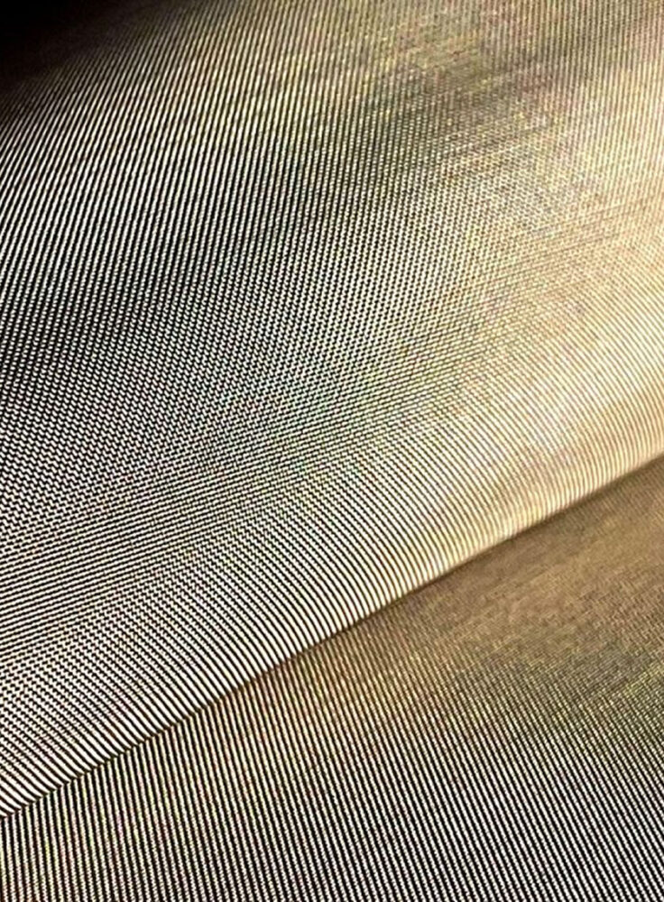 Primo piano su tessuto metallizzato a righe sottili, texture diagonale e variazioni di lucentezza tra colori beige e blu.