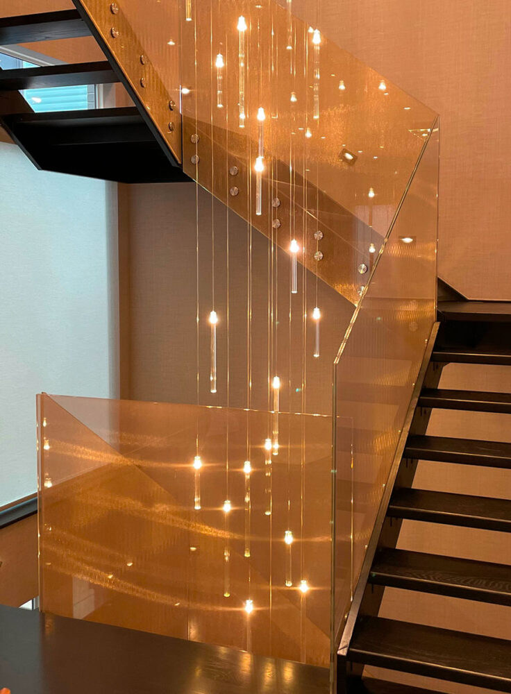 Interno moderno: scale in legno con balaustre in vetro e luci pendenti decorative che riflettono sulle superfici metalliche.