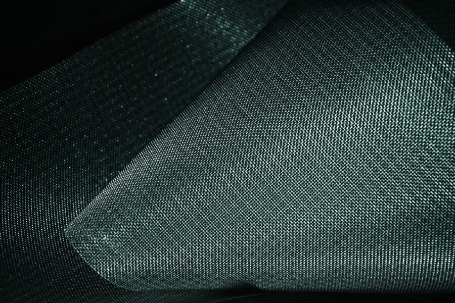 Primo piano su tessuto scuro e lucente, trama geometrica uniforme con riflessi verdi, texture tessile dettagliata e spigoli morbidi.