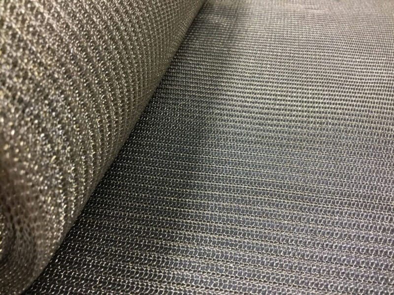 Primo piano su tessuto grezzo a spacchi sottili, filamenti metallici lucidi e trama a righe scure, texture ruvida e raffinata.