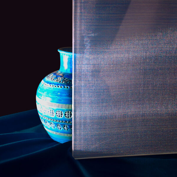 Vaso ceramico blu con decori geometrici disposto vicino a una parete riflettente, su sfondo scuro e tessuto blu.