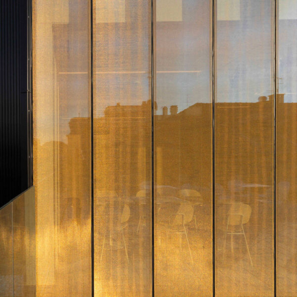 Facciata riflettente in vetri dorati con silhouettes di sedie e riflessi di edifici sopraelevati.