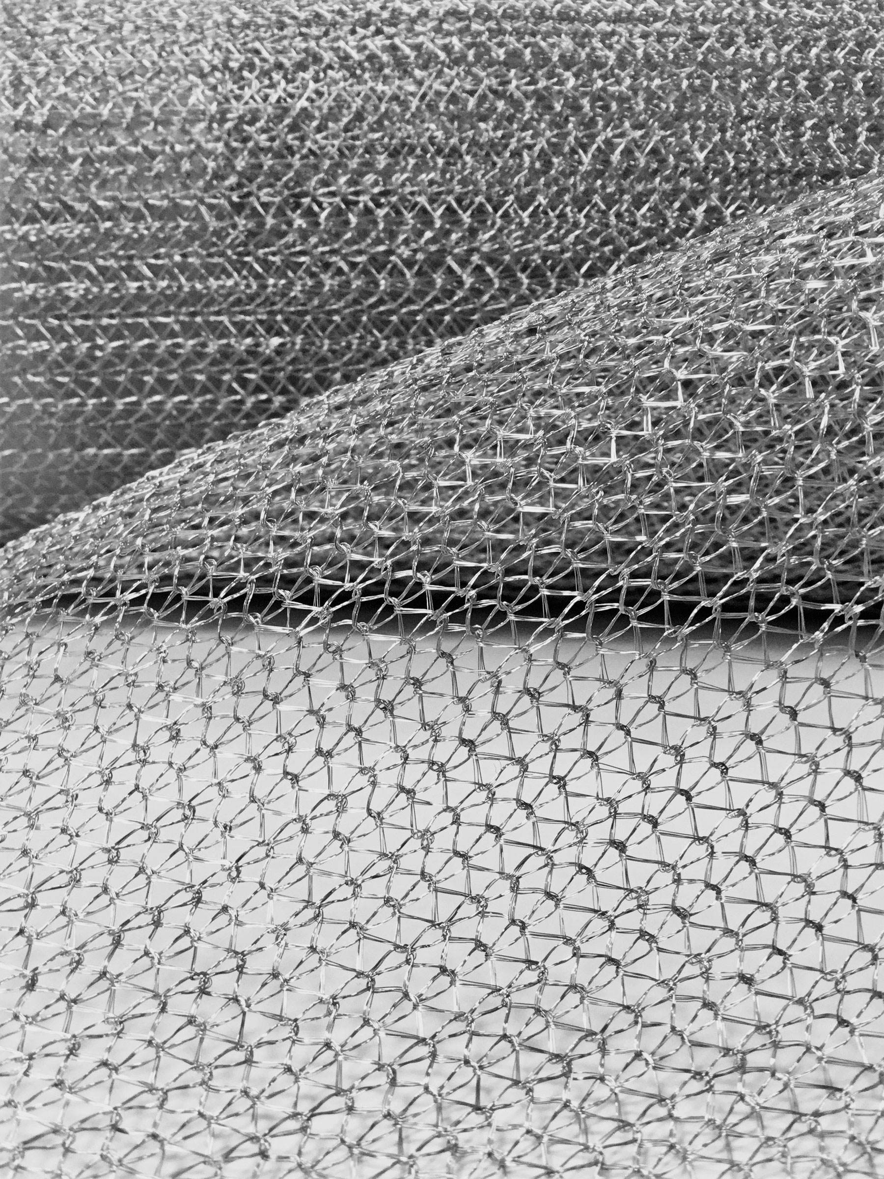 Rete metallica intrecciata a copertina, tessuto a maglie regolari che crea una texture.