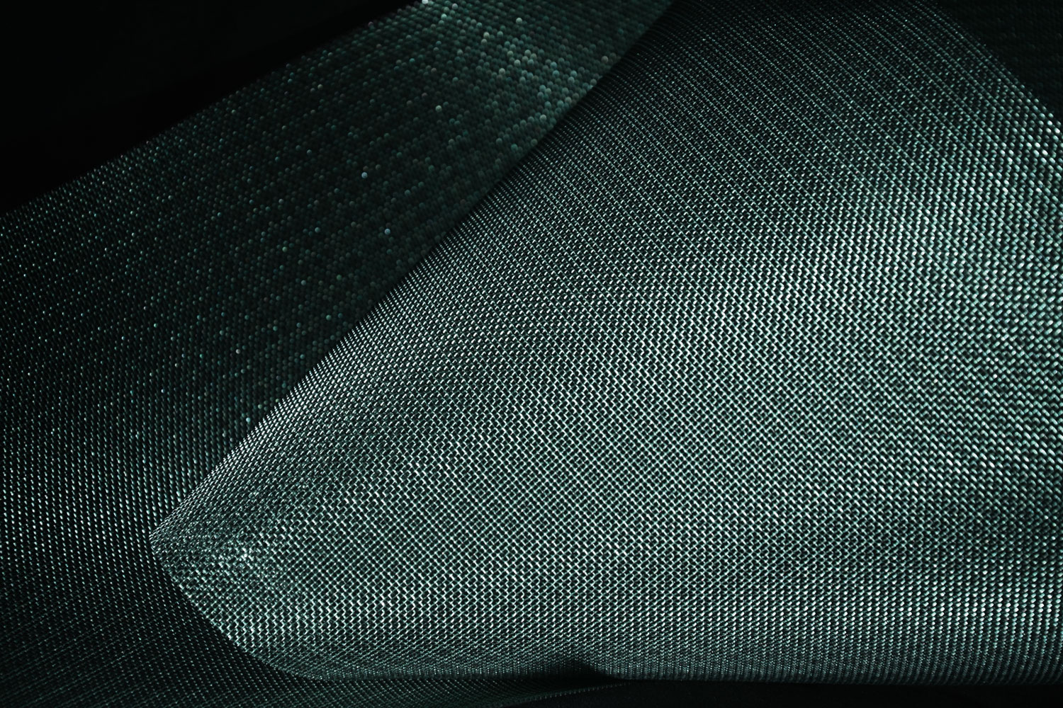 Primo piano su tessuto verde scuro, texture a trama fitta e pieghe morbide che creano contrasti di luci e ombre.