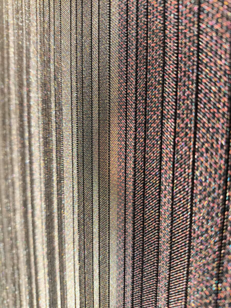 Dettaglio di fili tessuti intrecciati in tonalità metalliche e tinte scure, mostrando texture fibrose e motivi rigati.