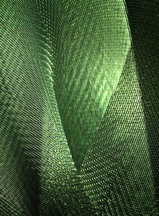 Tela di rete metallizzata verde intrecciata, texture a fisheye che crea pieghe e profondità, riflessi luminosi e pattern geometrici.
