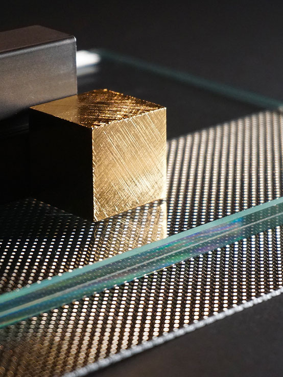 Moderno cubo di legno lucido in primo piano su superficie metallica testurizzata, riflessi dorati e linee trasparenti sullo sfondo.