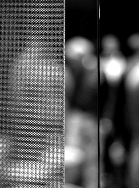 Dettaglio in primo piano di una superficie metallica perforata con riflessi sfocati sullo sfondo, effetto bokeh in bianco e nero.