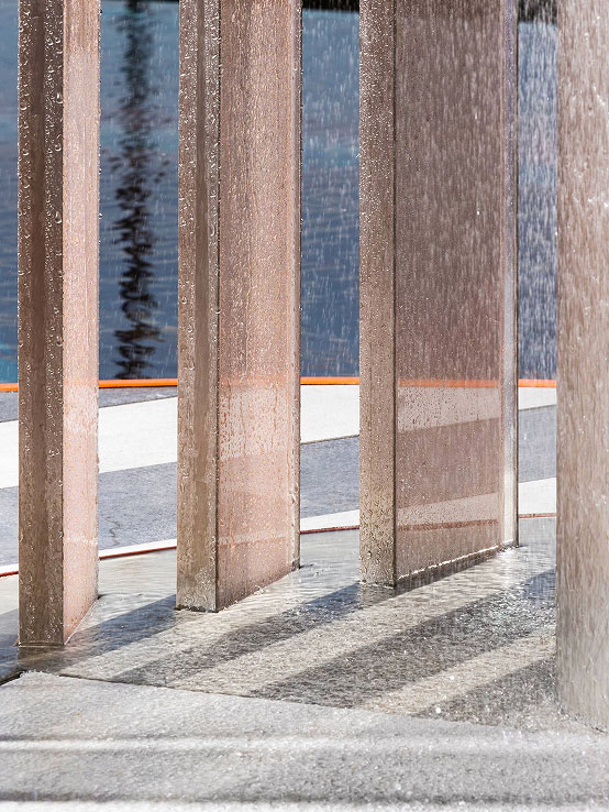 Sottile vasca d'acqua con colonne verticali in tessuti metallizzati, riflessi e pavimento umido, atmosfera minimalista e linee pulite.